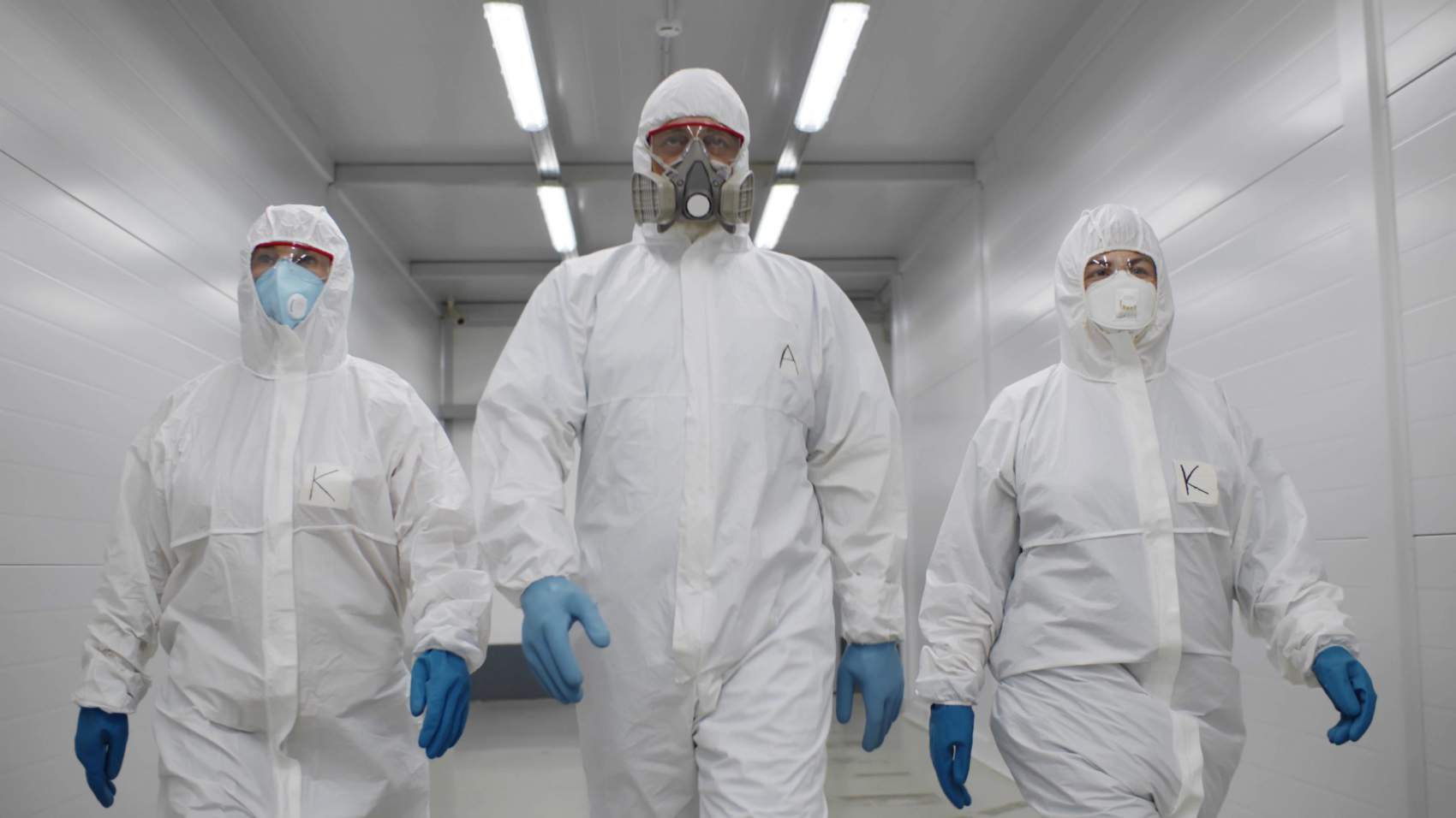 Team of virologists in hazmat suits walking in corridor to do disinfection. Specialists in protective overalls and respiratory mask walking in hallway of industrial building or hospital